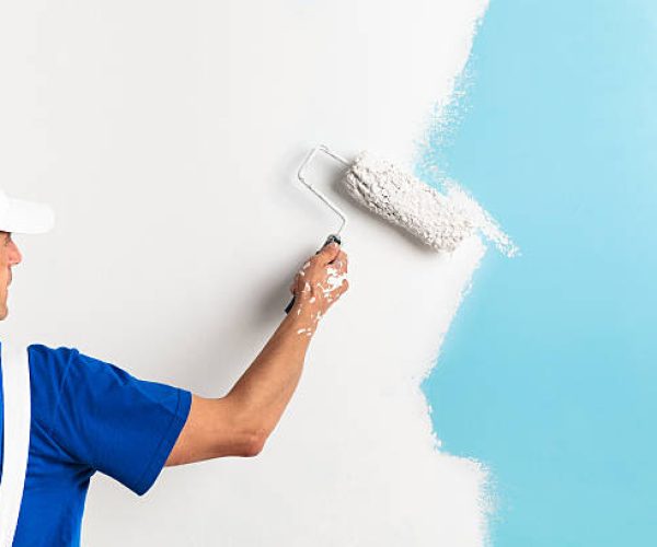 Back view of painter painting a wall with paint roller, with copy space